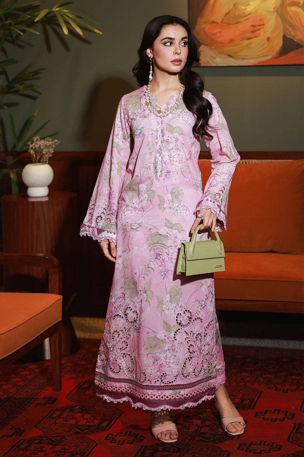 Woman in a pink floral dress holding a green handbag in an indoor setting.