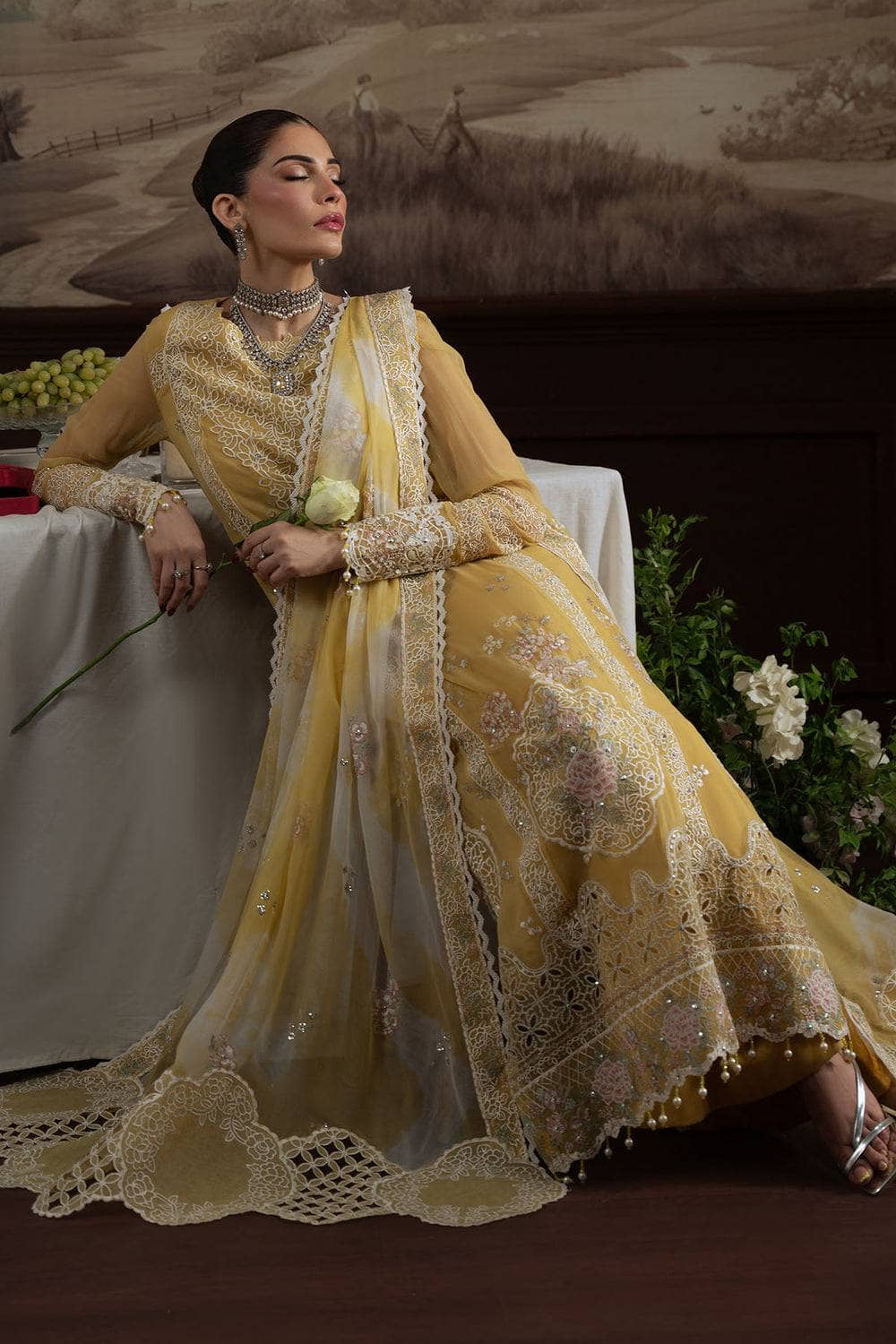 Woman in a yellow embroidered traditional outfit sitting in a decorative setting.