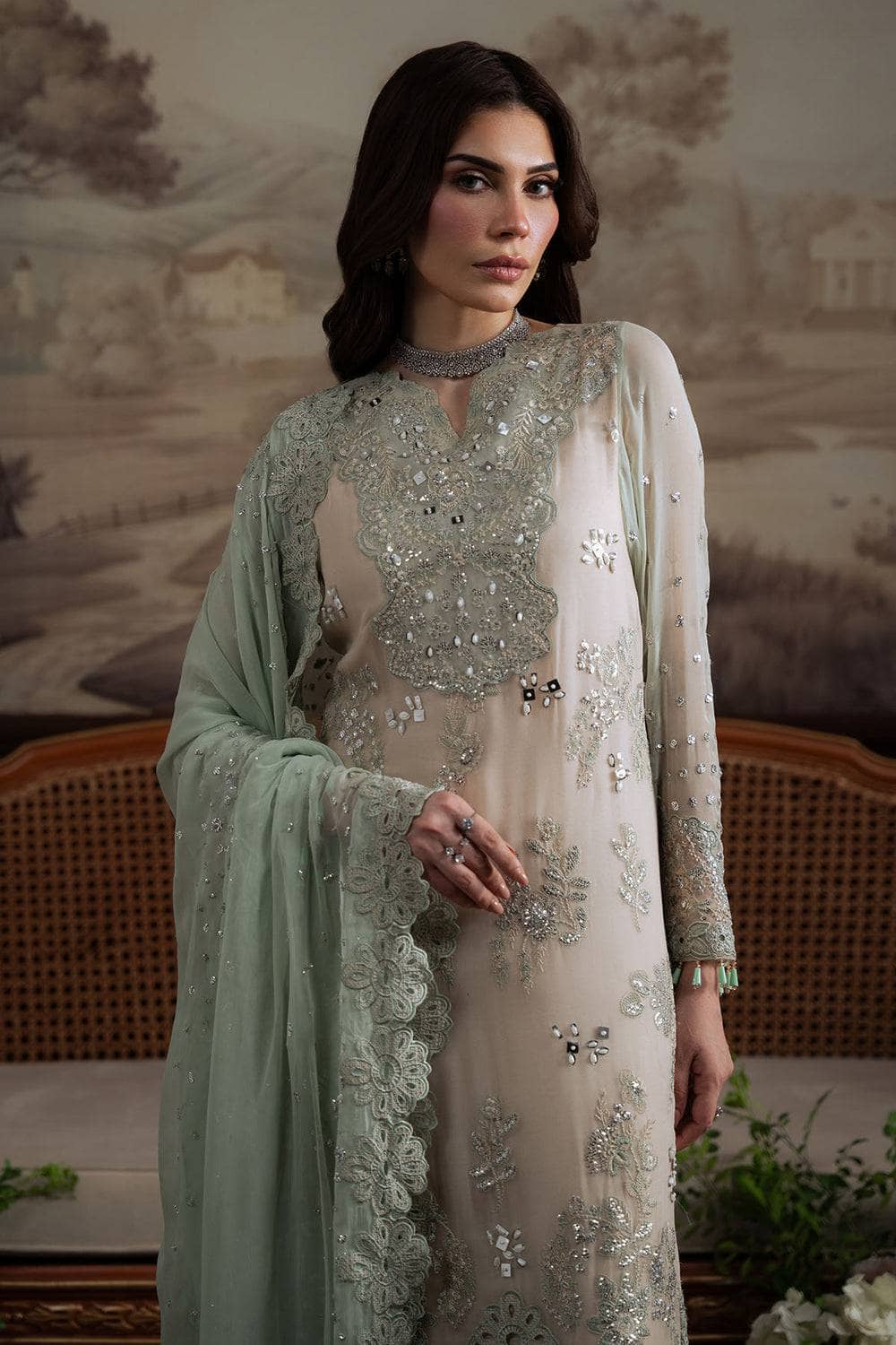 Woman wearing an embroidered light green dress with a matching dupatta in a decorative setting.