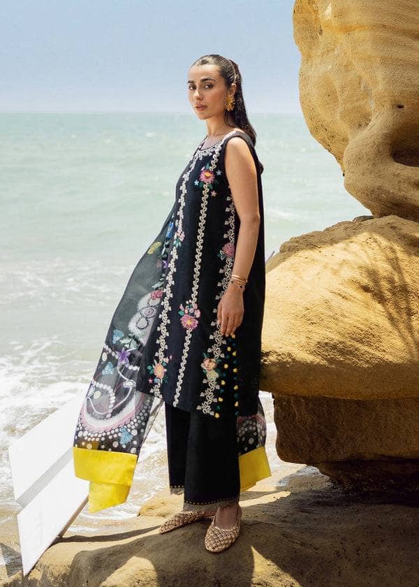 Woman in traditional outfit standing on a rocky beach with ocean in the background