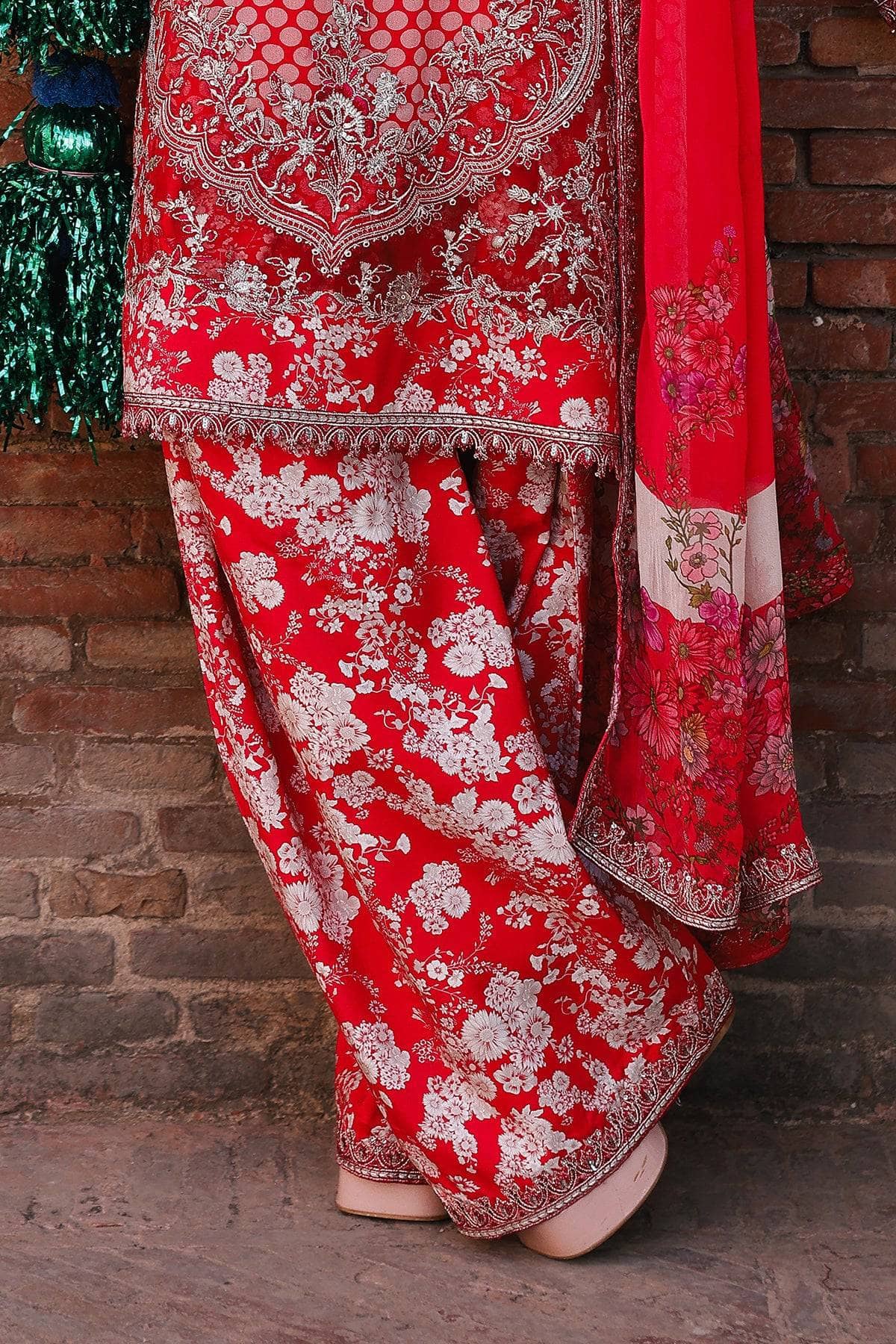 Red traditional outfit with white floral patterns against a brick wall.