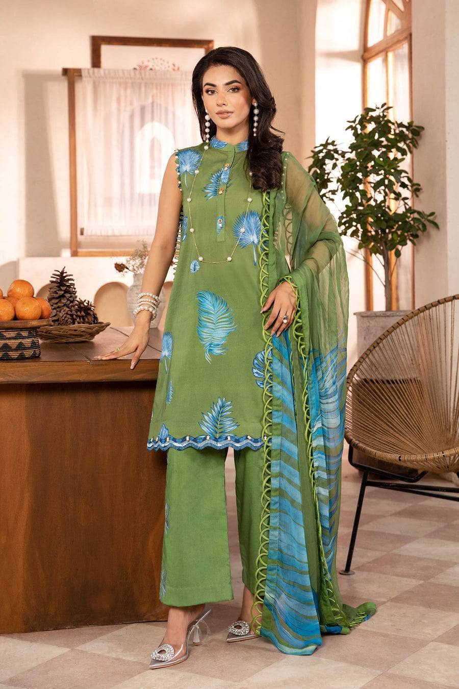 Woman wearing a green and blue embroidered outfit in an indoor setting.