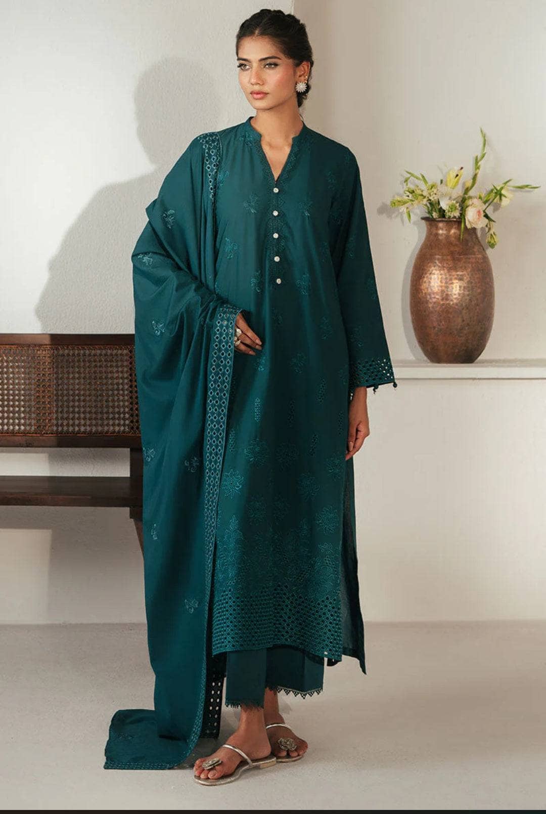 Woman wearing a teal traditional outfit with a matching dupatta in a minimalistic setting.