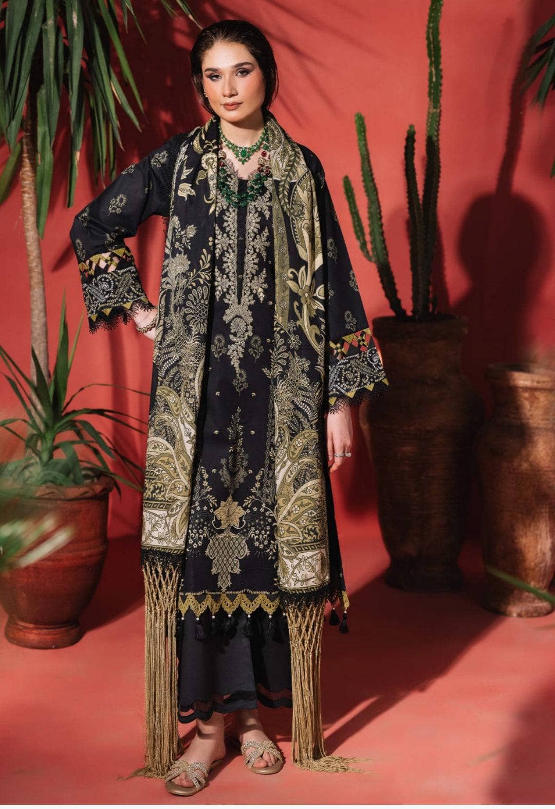 Woman wearing a black and gold embroidered outfit with plants in the background