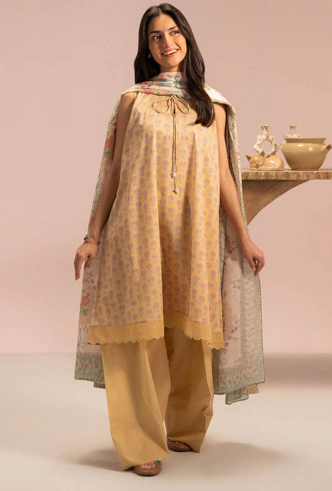 Woman wearing a beige traditional outfit with a patterned dupatta against a pink background