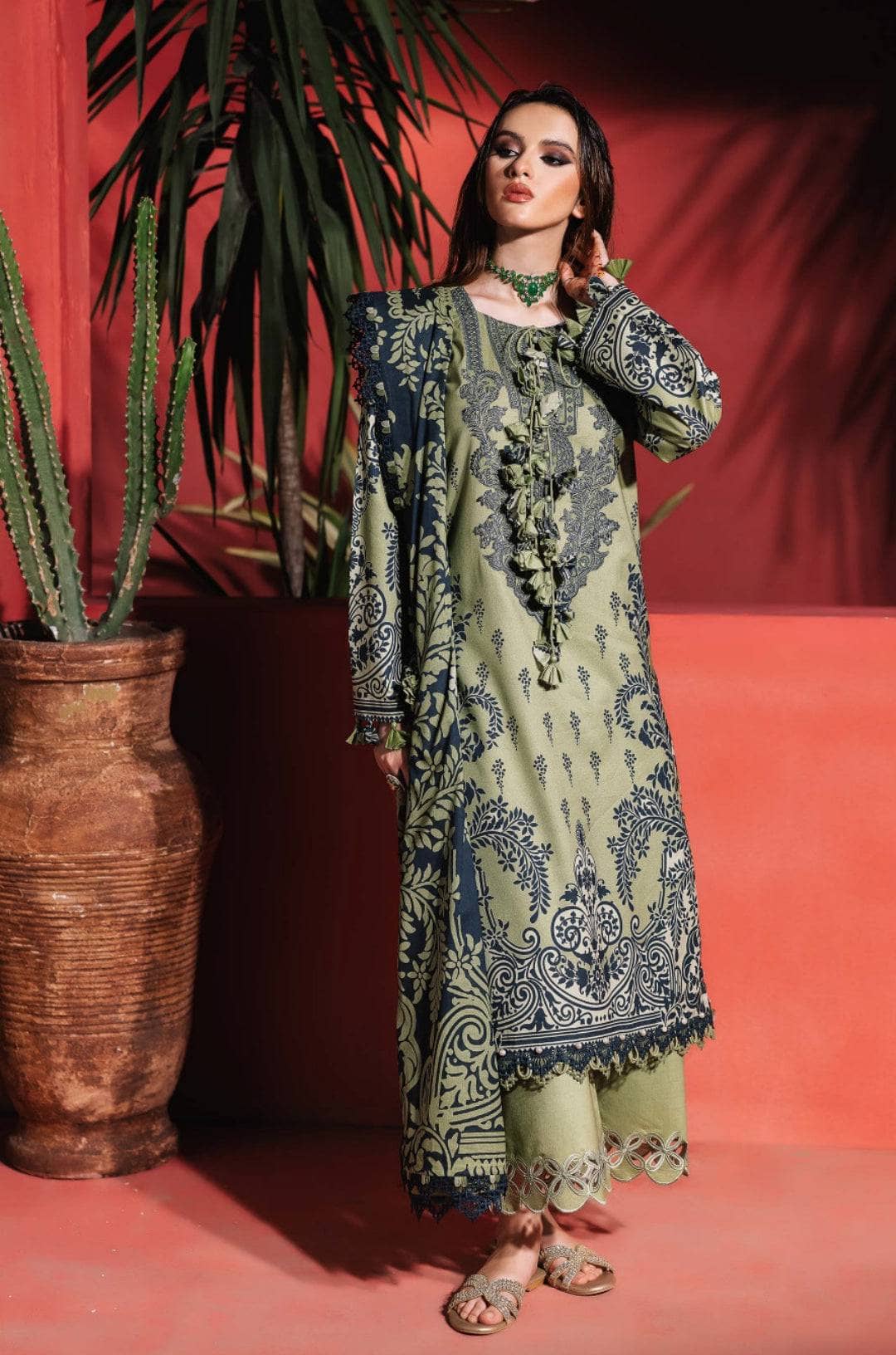 Woman in a patterned outfit standing against a red wall with a plant.