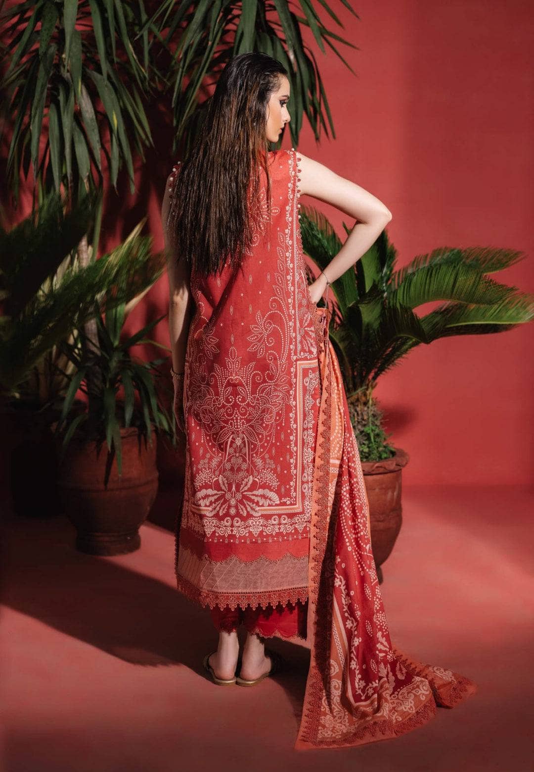 Woman in a red patterned dress standing against a red background with plants.