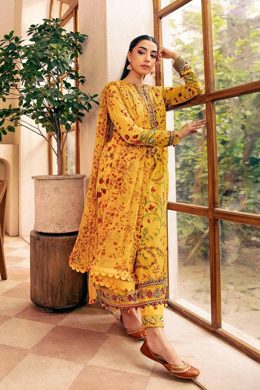 Woman in a yellow floral outfit standing by a window with greenery outside