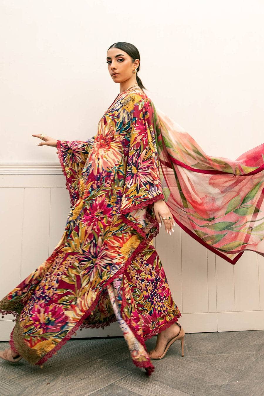 Woman wearing a colorful floral outfit with a flowing scarf against a neutral background
