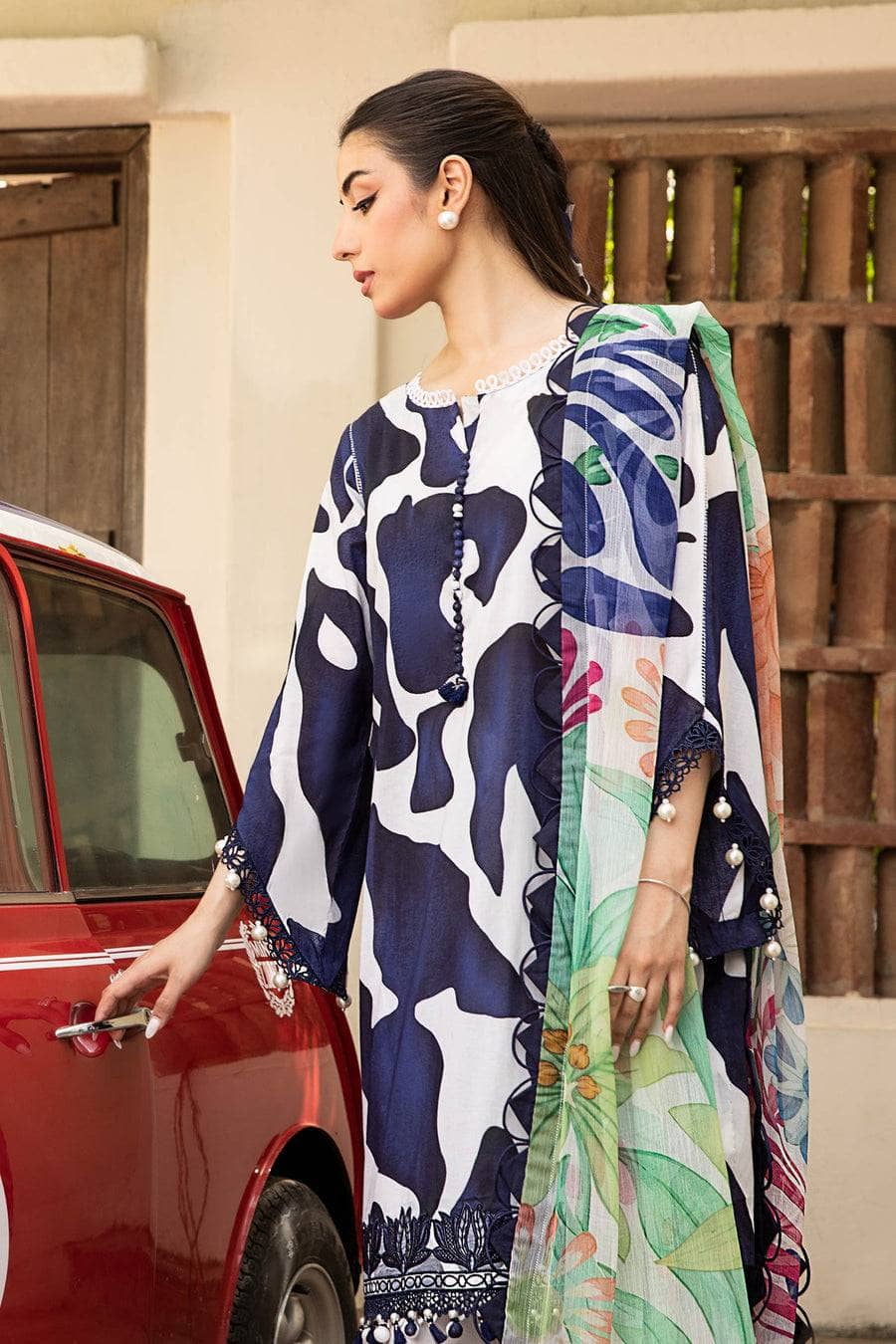 Woman in a patterned outfit opening a car door, with a decorative wooden gate in the background.