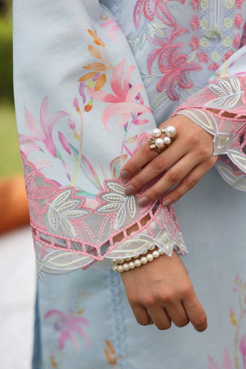 Close-up of a hand wearing pearl jewelry with floral embroidery on a garment.