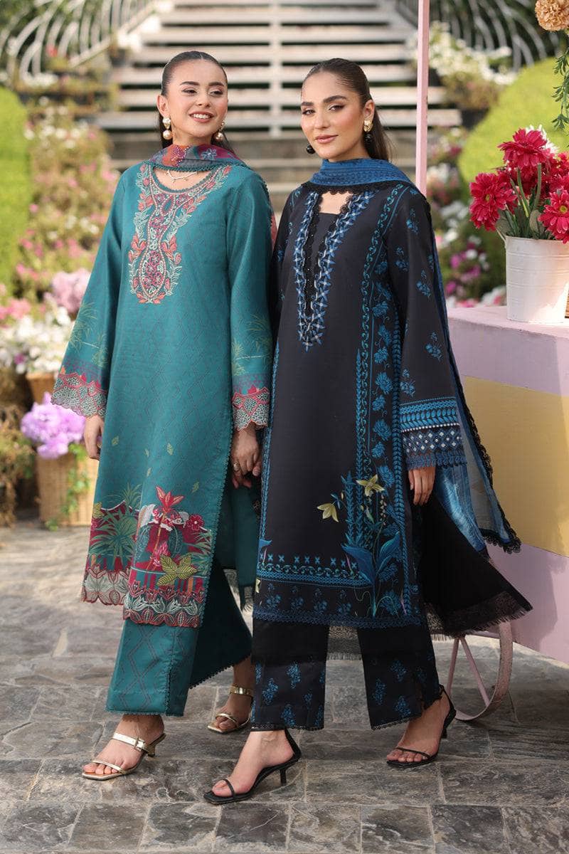 Two women in traditional embroidered outfits standing outdoors with flowers and a building in the background.