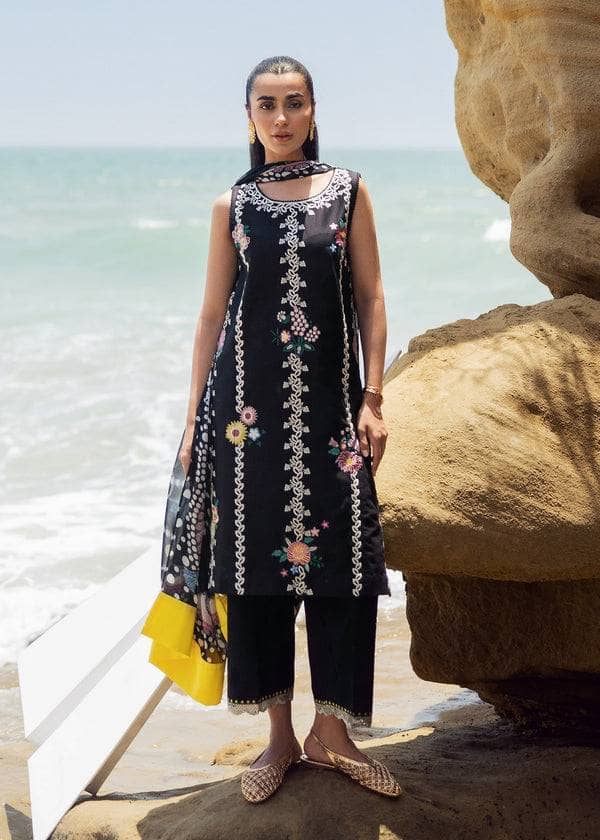 Woman in a black embroidered dress standing on a rocky beach with ocean in the background