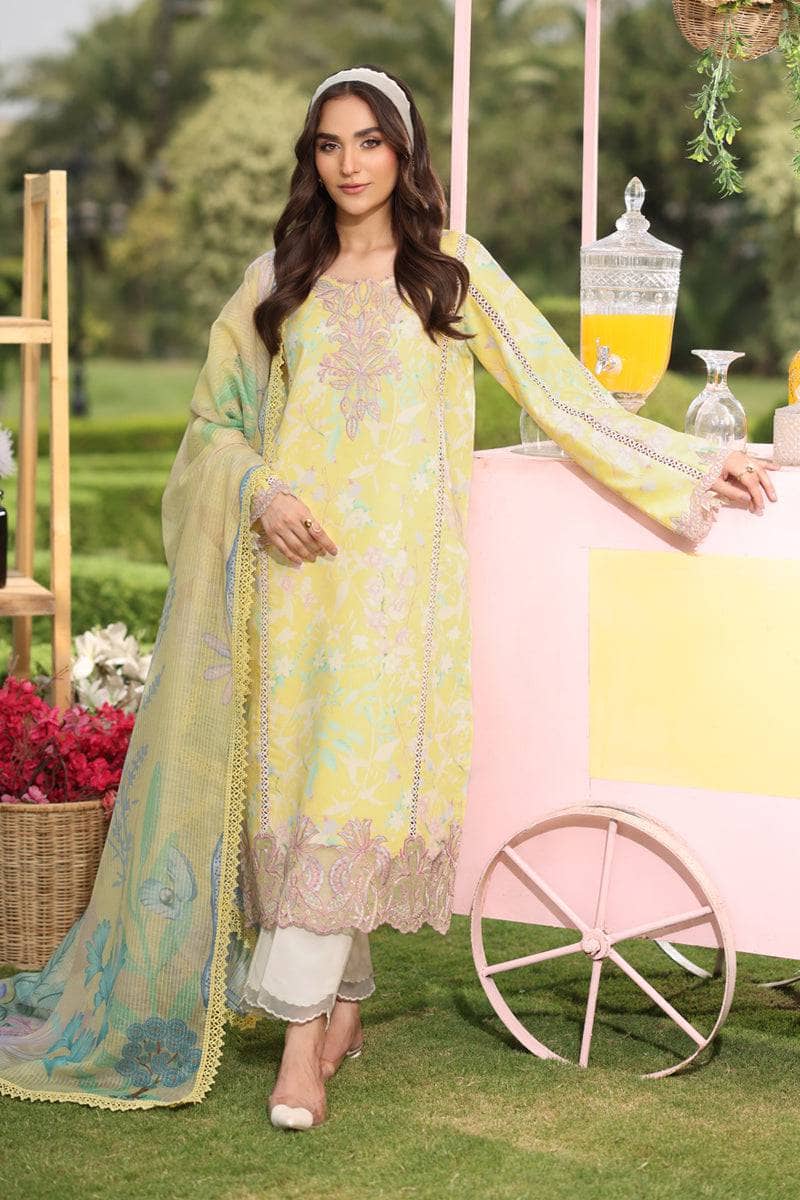 Woman in a light green embroidered outfit standing outdoors with a decorative cart and flowers in the background.