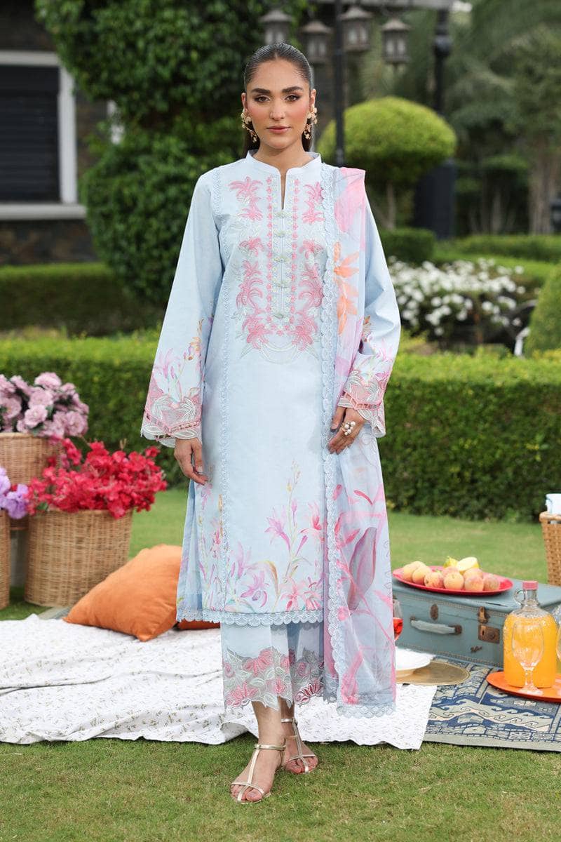 Woman in a light blue embroidered outfit standing outdoors with flowers and a table in the background