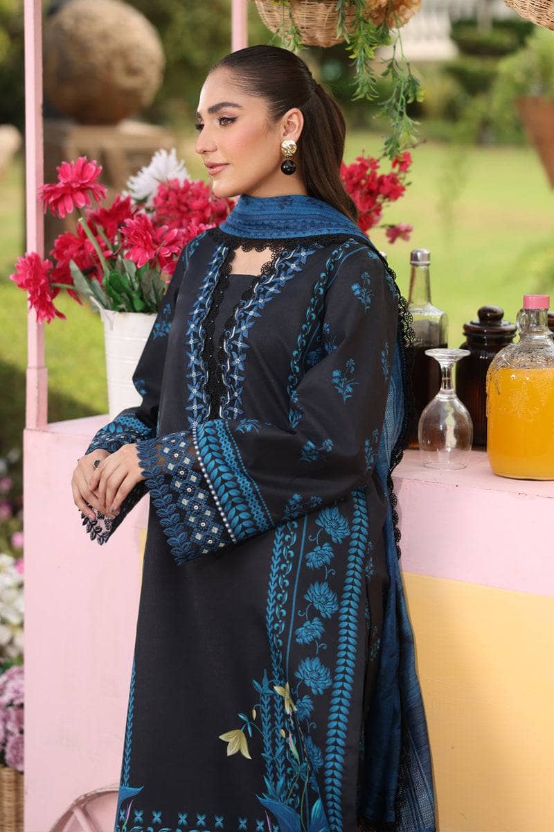 Woman in a black and blue embroidered outfit standing outdoors with flowers and bottles in the background