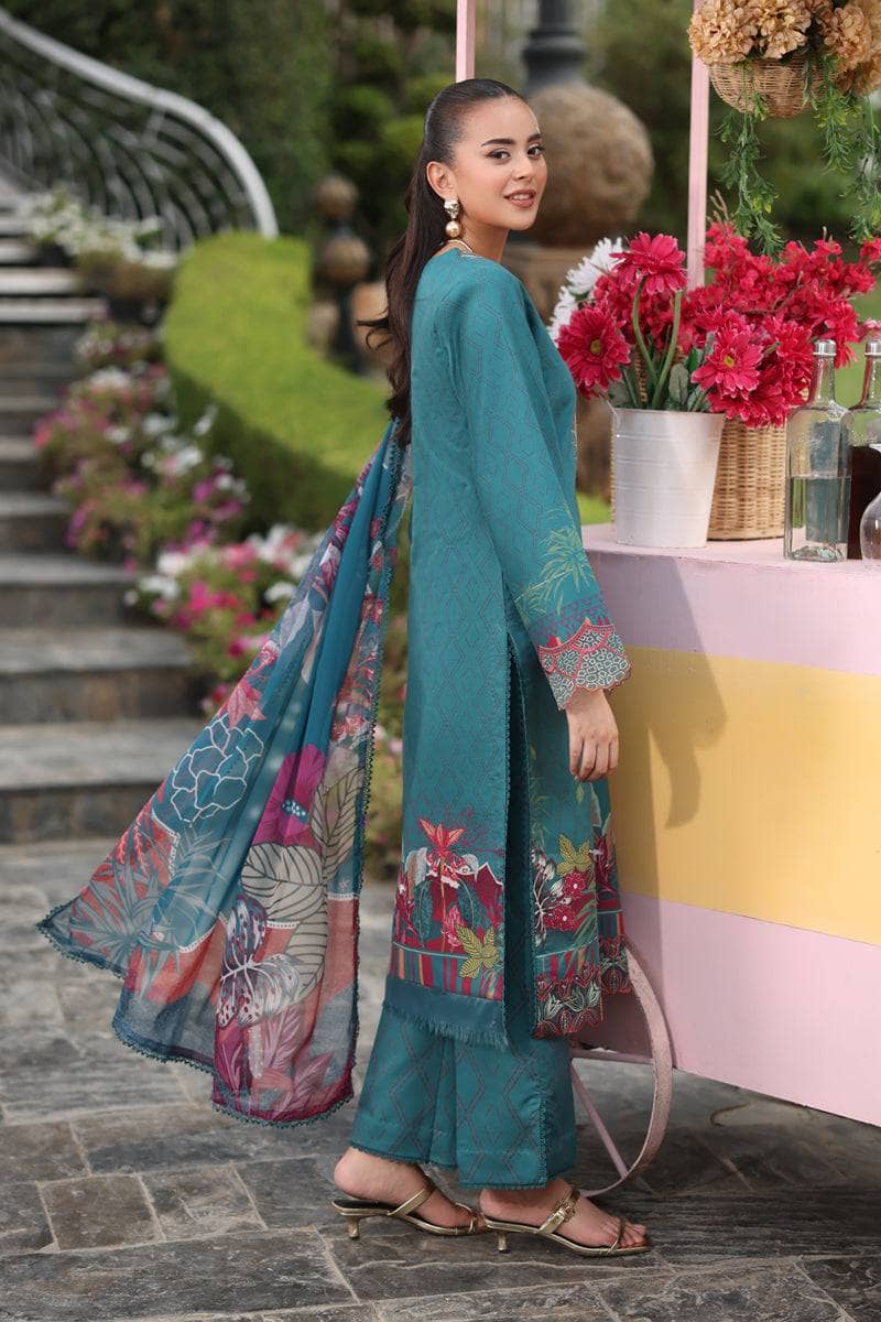 Woman in teal traditional outfit with floral patterns standing outdoors near a colorful table.