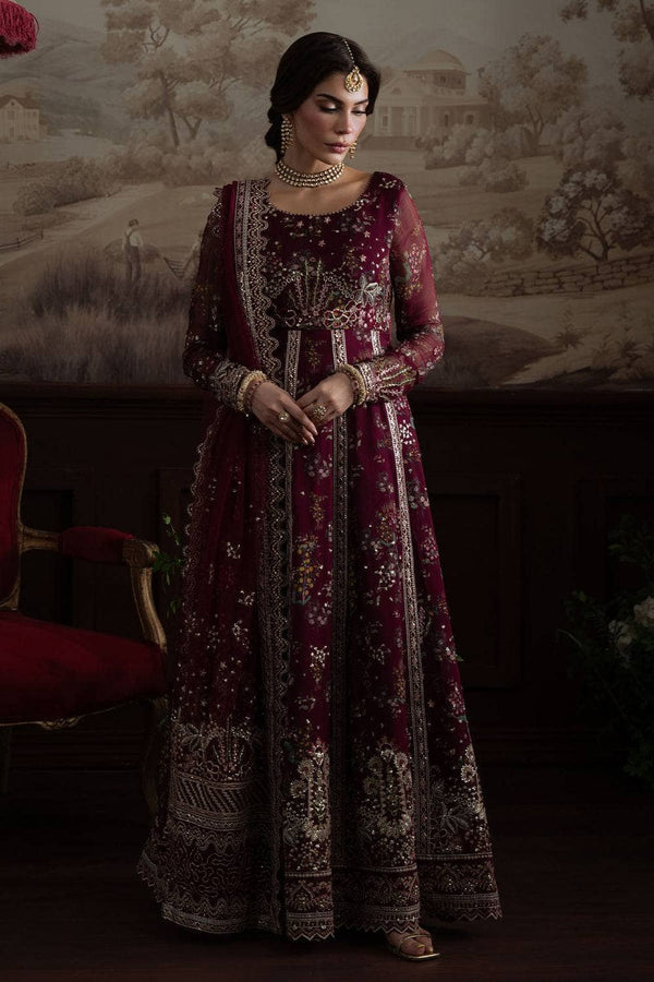 Woman in a maroon embroidered traditional outfit standing against a decorative wall.