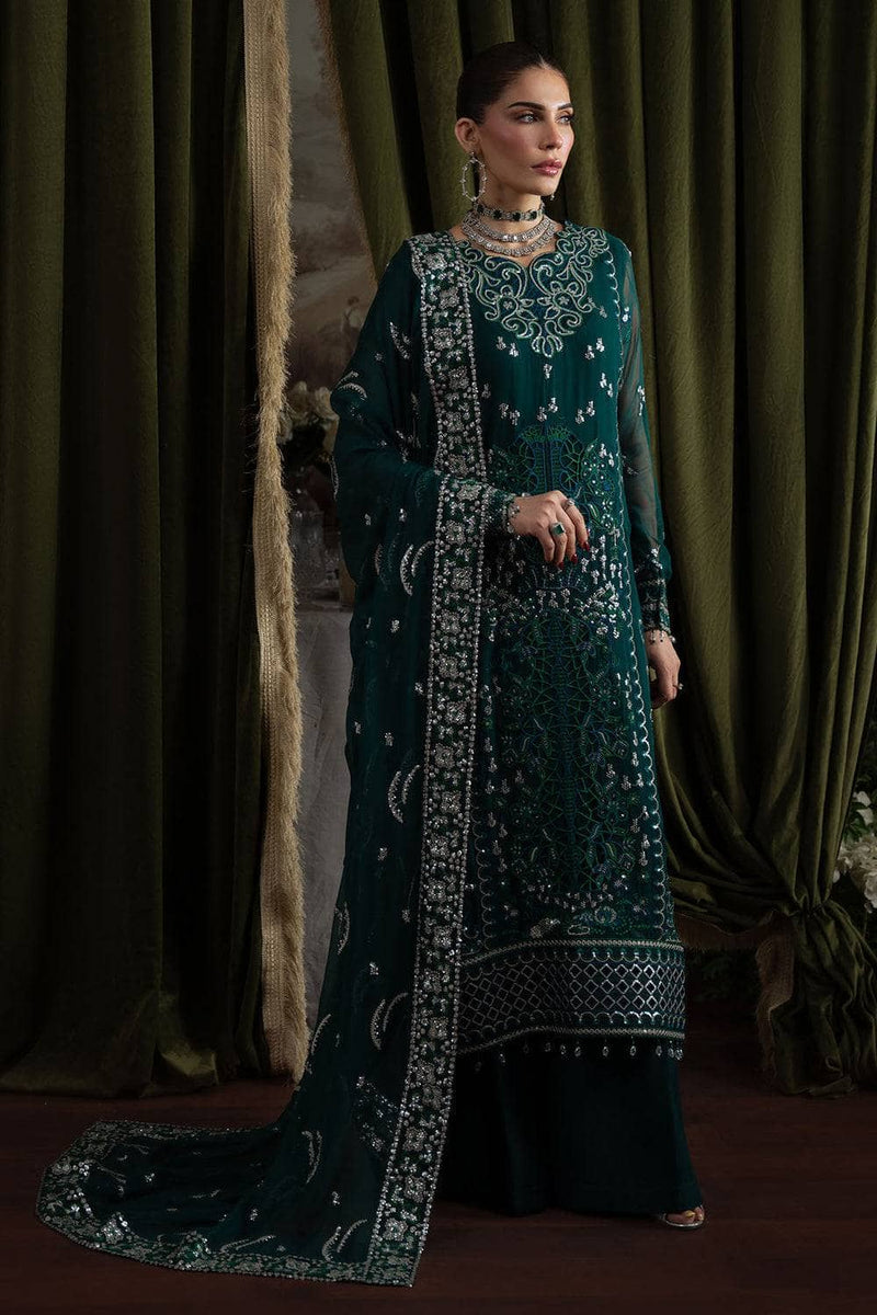 Woman in a dark green embroidered traditional outfit standing against a draped curtain.