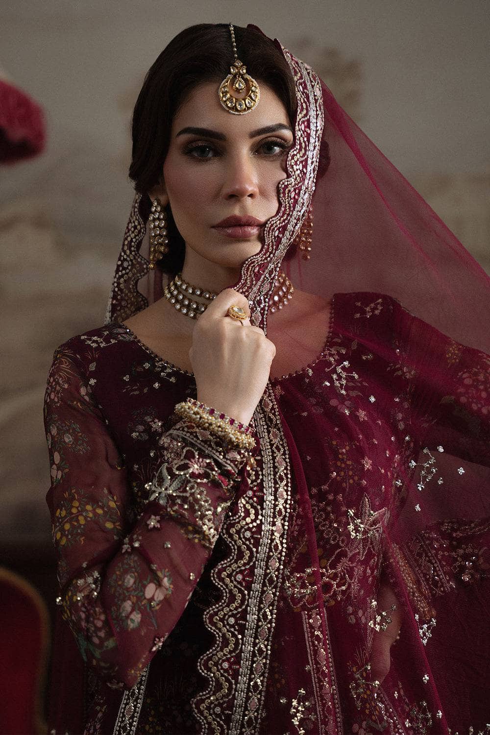 Woman in traditional embroidered outfit with a veil, wearing jewelry.