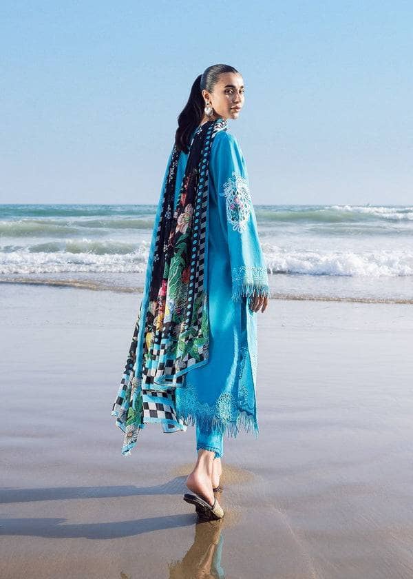 Woman in a blue dress with a patterned scarf standing on a beach.