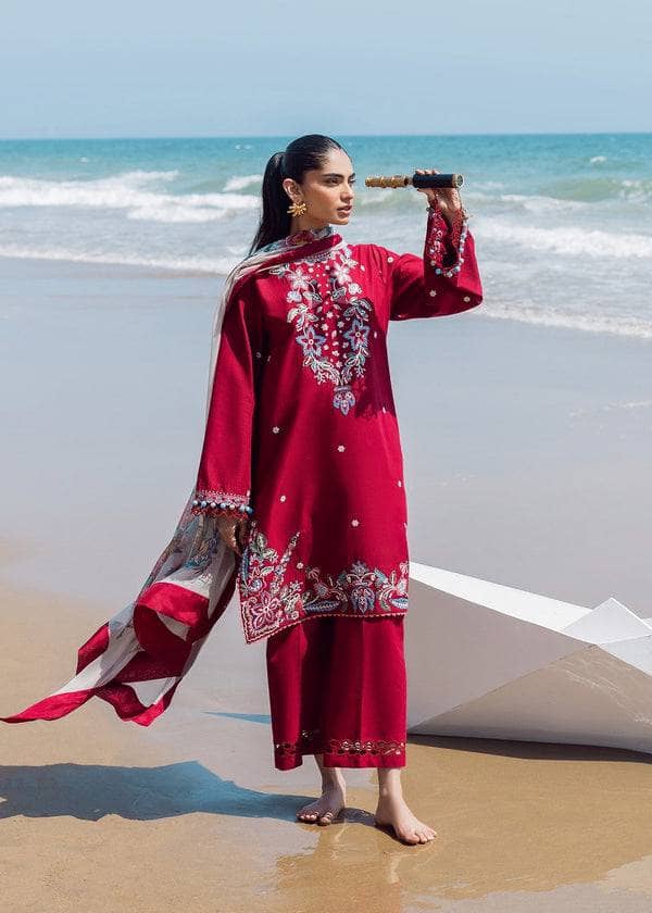 Woman in a red traditional outfit standing on a beach with ocean waves in the background