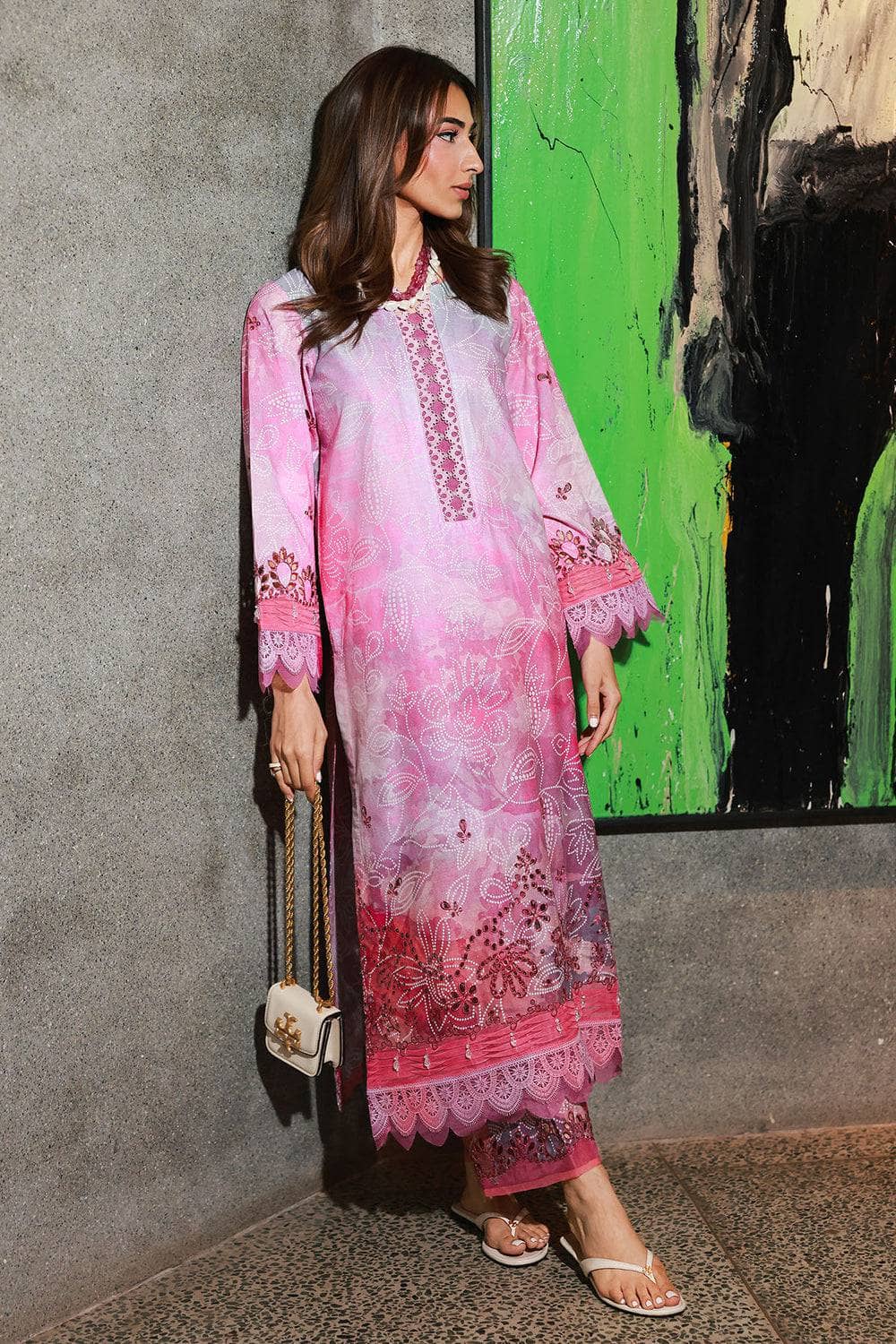 Woman in a pink embroidered outfit standing against a colorful wall.