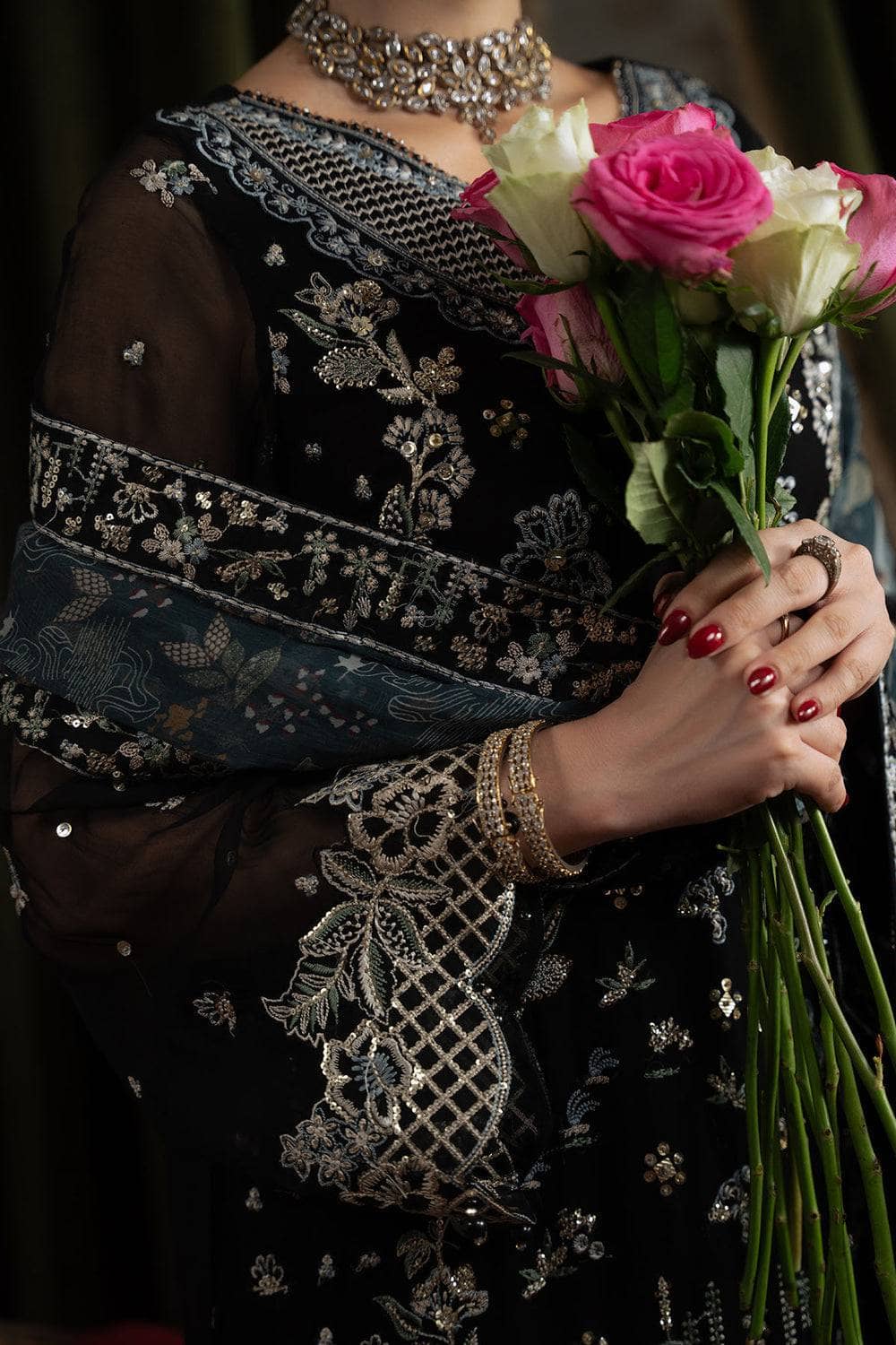 Person wearing a black embroidered saree holding pink and white roses.