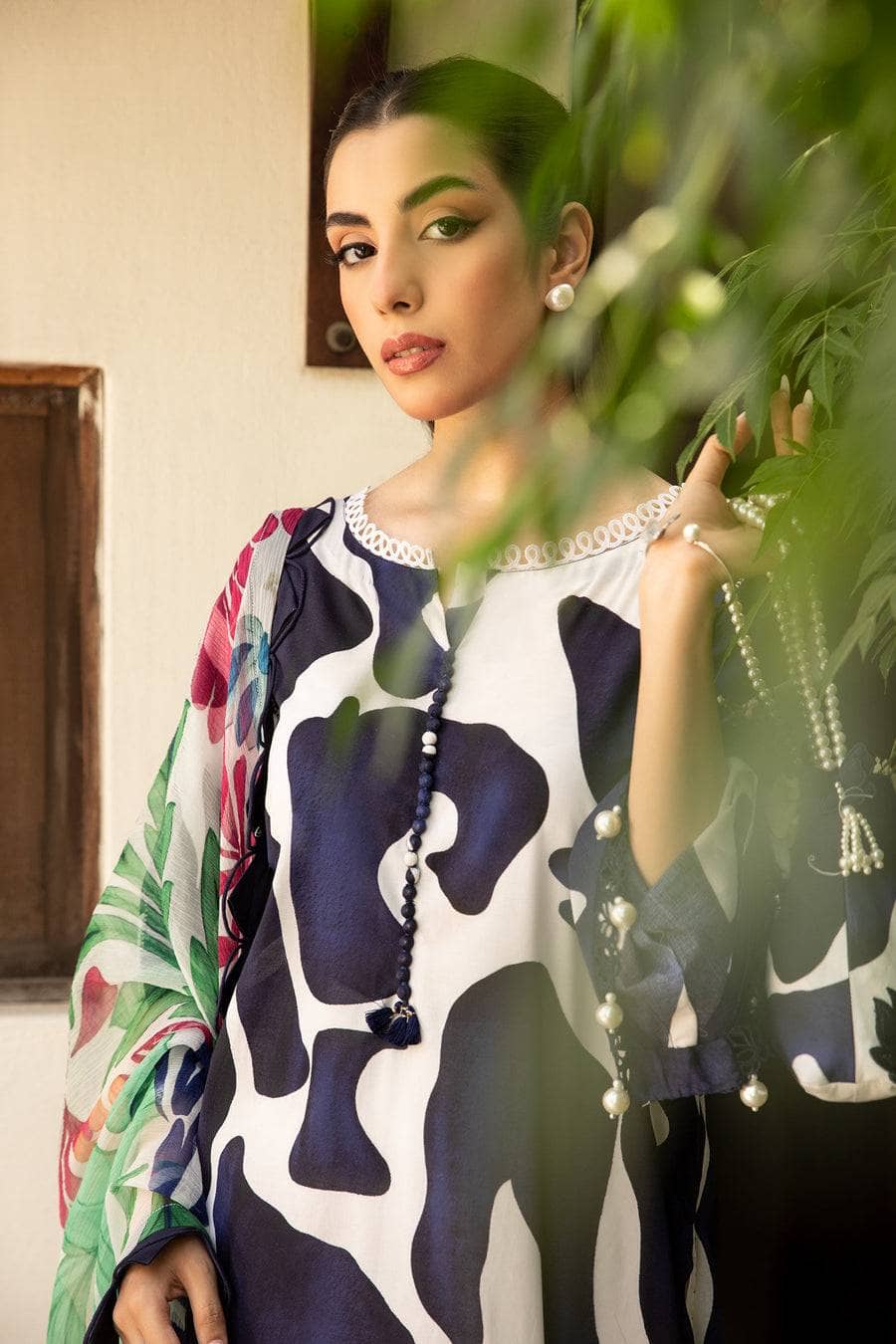 Woman wearing a patterned blouse with a plant in the foreground