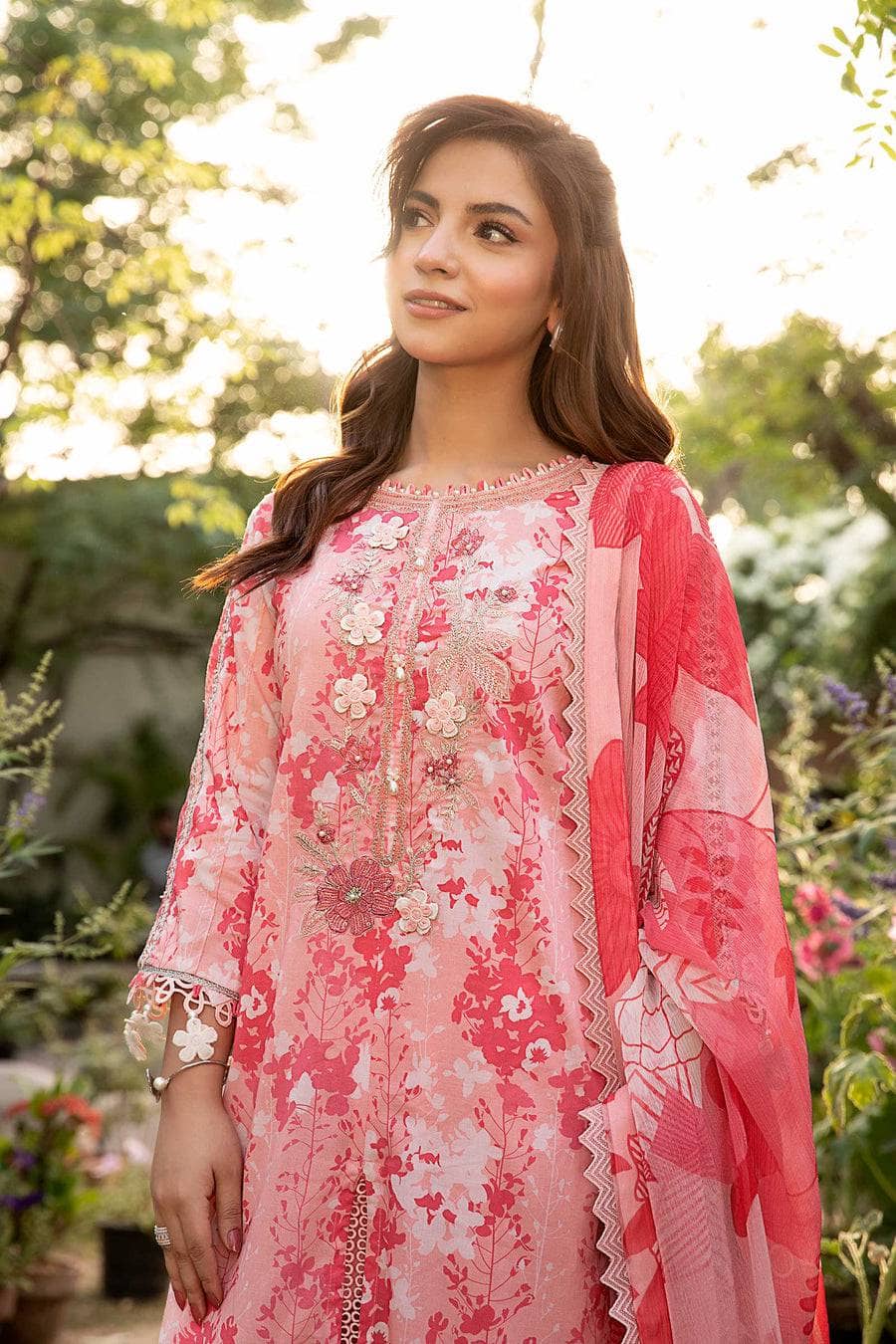Woman wearing a pink floral dress with a matching dupatta in an outdoor setting.