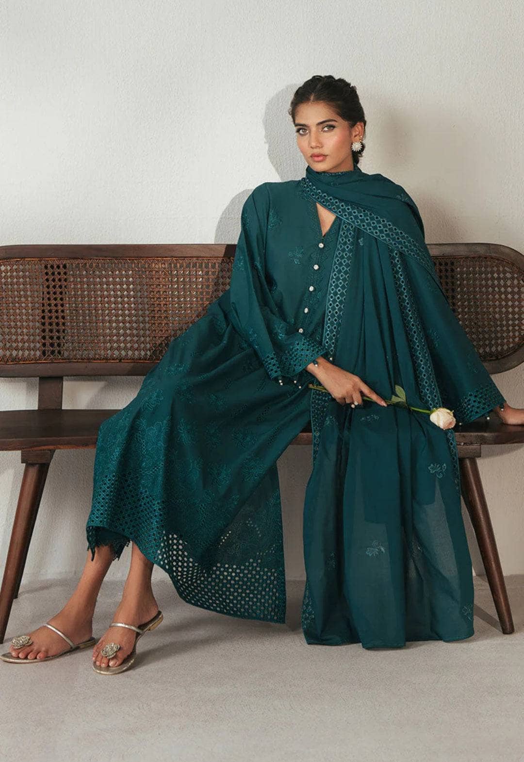 Woman in a teal outfit sitting on a wooden bench holding a white flower.