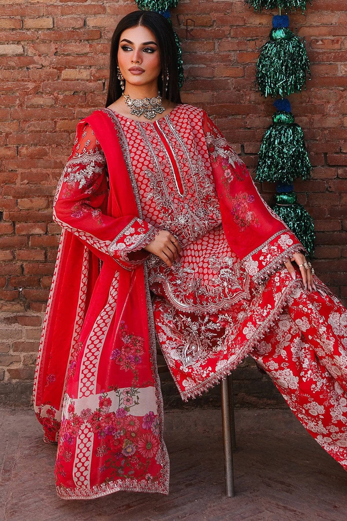 Red embroidered traditional outfit displayed against a brick wall with decorative elements.
