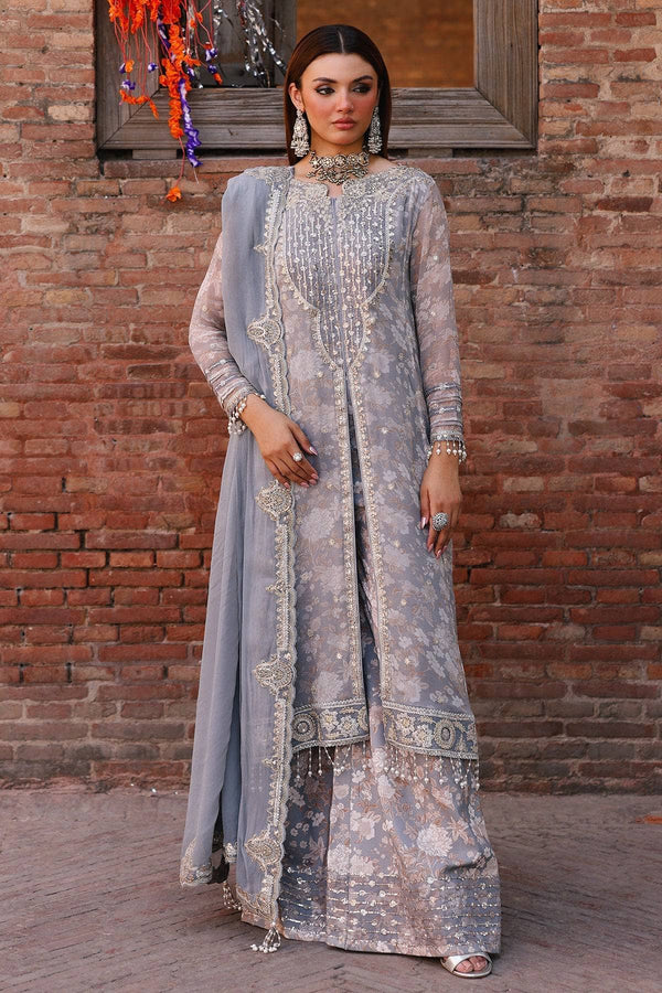 Woman in a light blue embroidered traditional outfit standing against a brick wall.