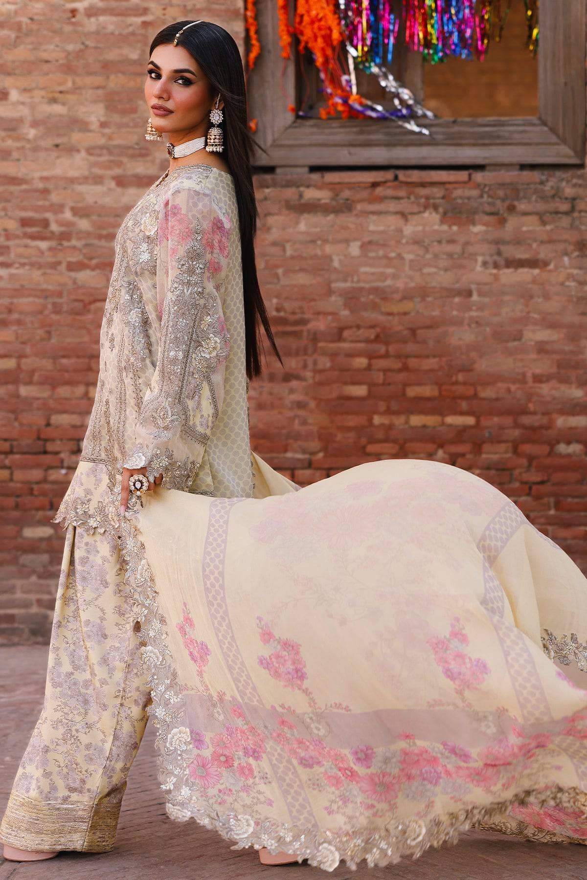 Woman in traditional embroidered outfit standing next to a white cow against a brick wall.
