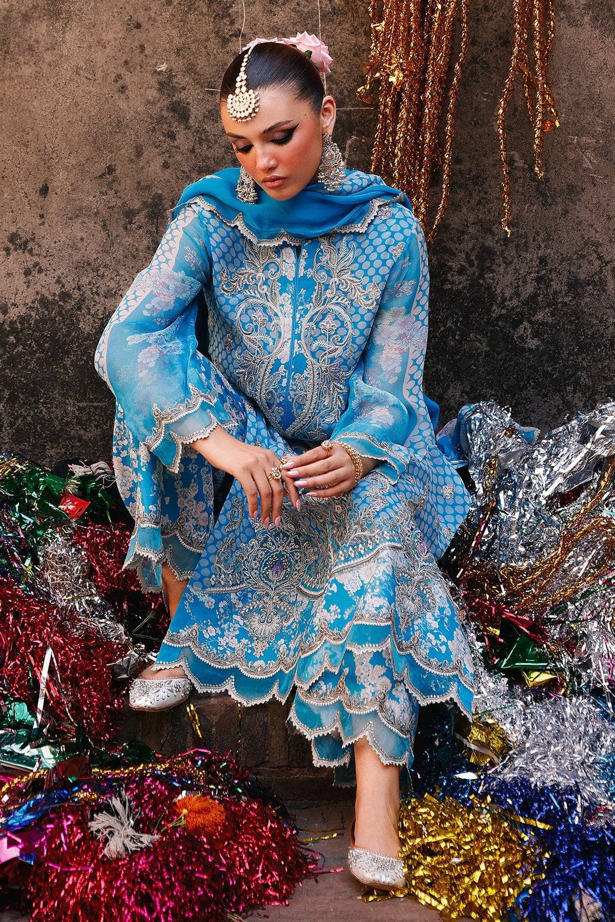Woman in a blue embroidered dress sitting amidst colorful tinsel