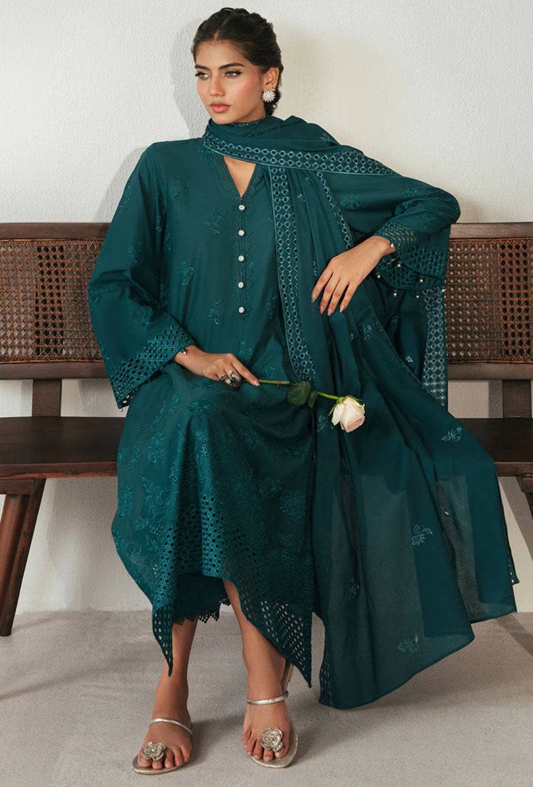 Woman wearing a teal traditional outfit with a matching dupatta, holding a white flower, against a white background.