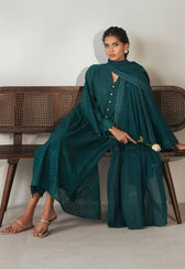 Woman in a teal outfit sitting on a wooden bench holding a white flower.