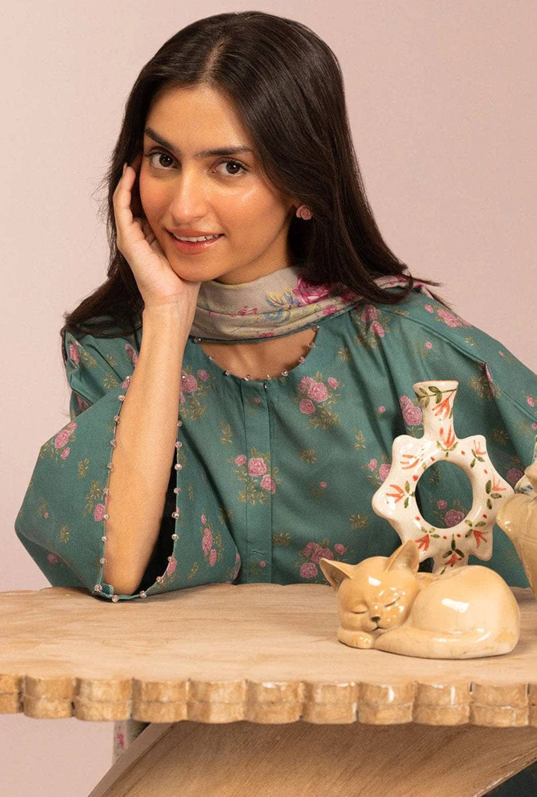 Woman in a floral blouse sitting behind a wooden table with decorative items.