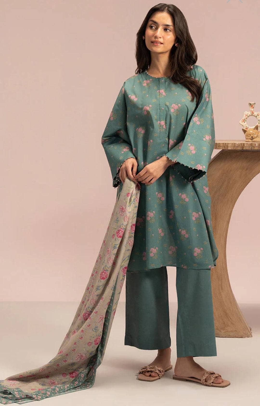 Woman wearing a teal floral outfit with a matching dupatta against a pink background