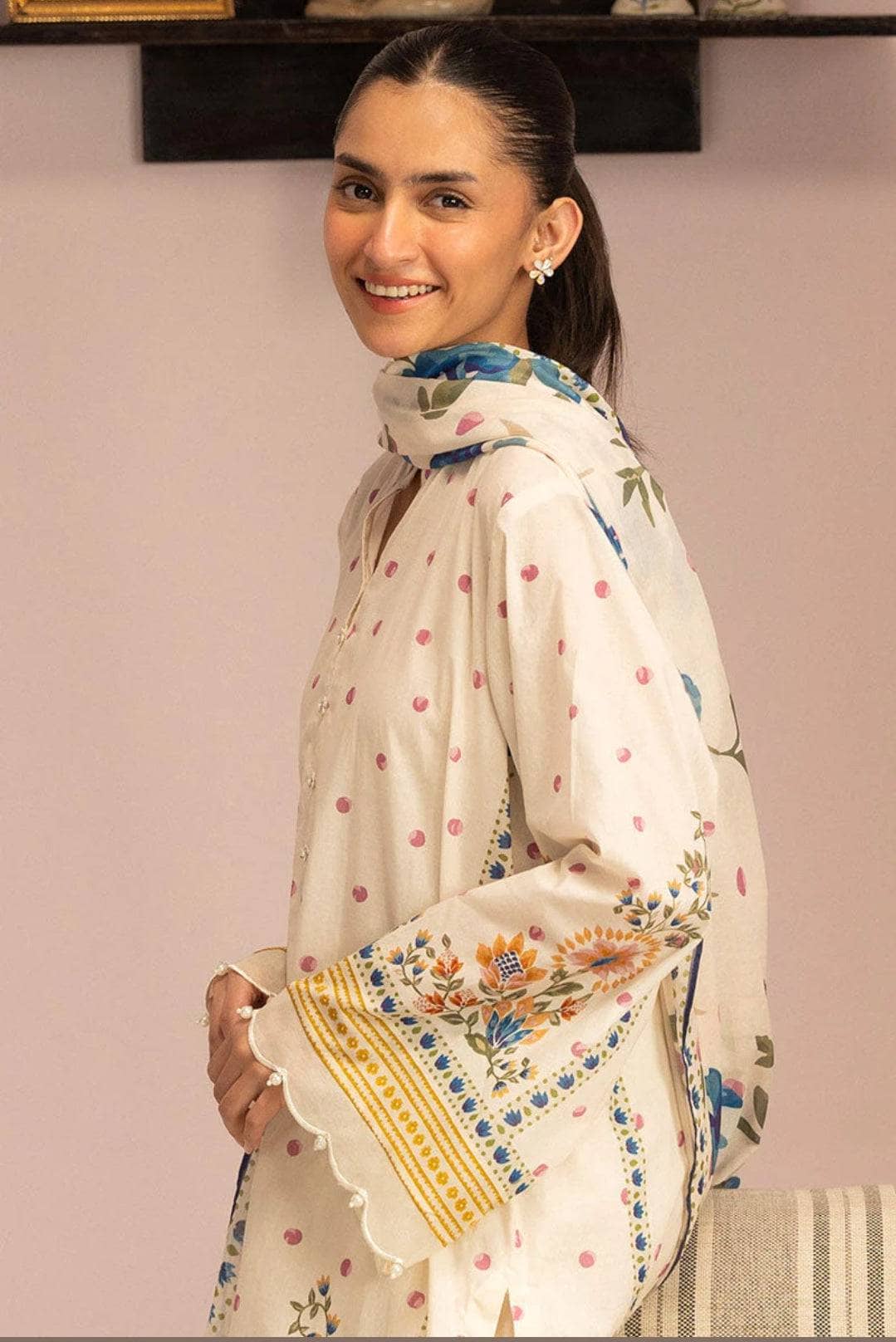 Woman wearing a traditional outfit with a floral shawl against a plain background
