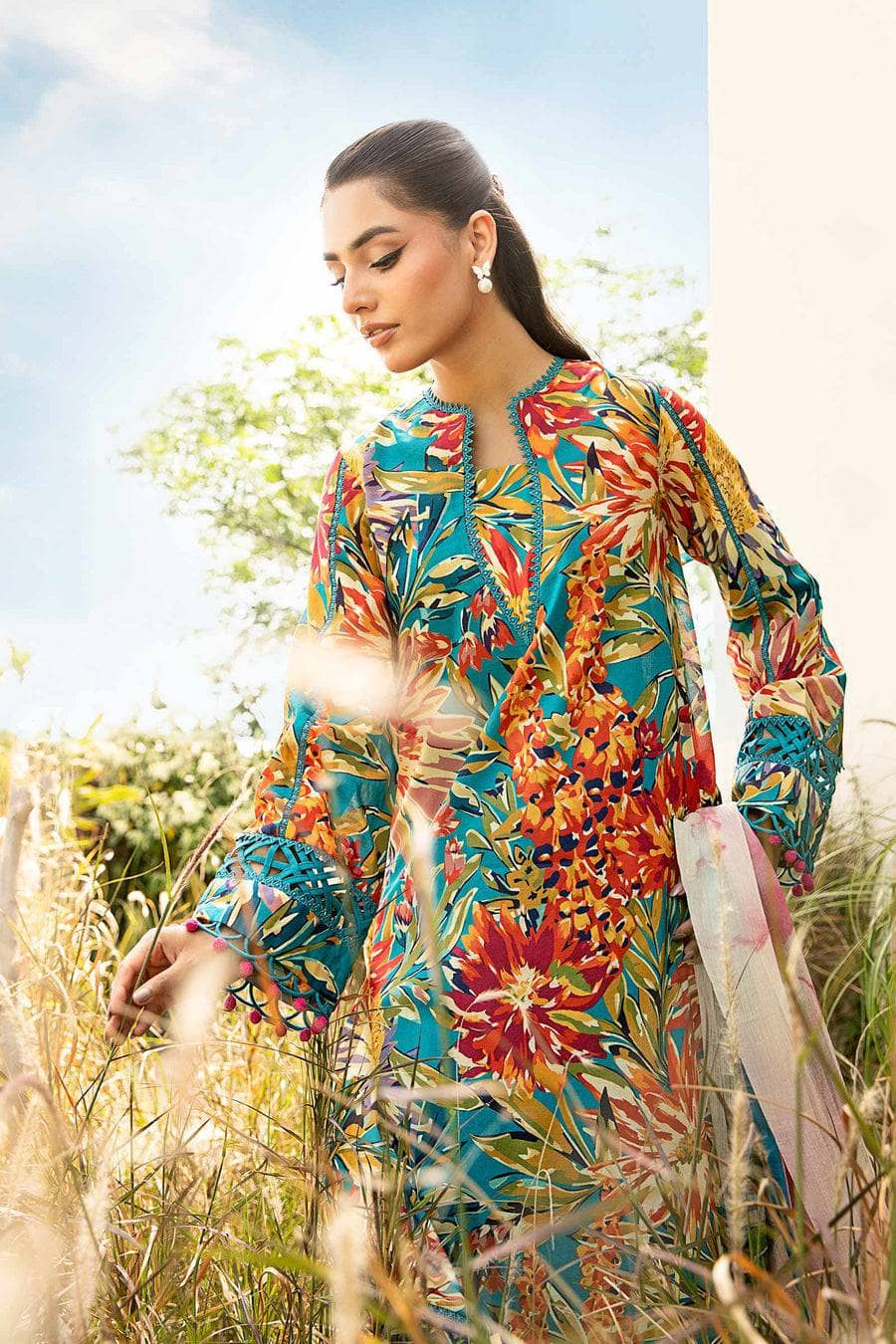 Woman in a colorful floral dress standing in a field with a clear sky.