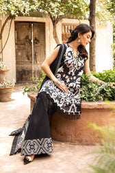 Woman in black and white patterned outfit sitting outdoors with greenery and a wooden door in the background
