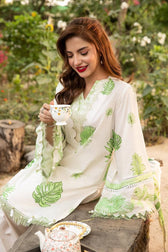 Woman in a white and green dress sitting outdoors with a cup of tea.