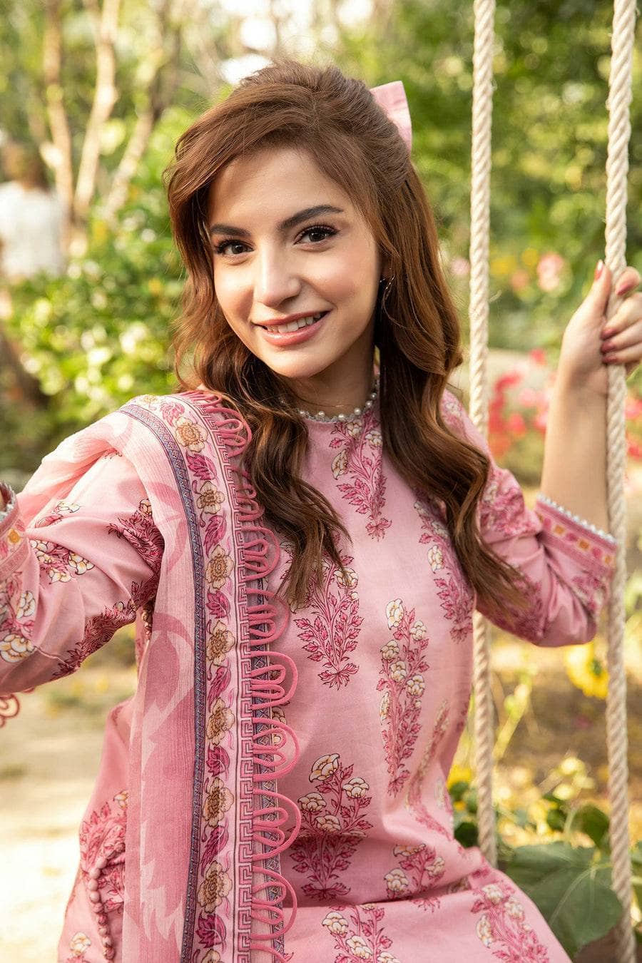 Woman in a pink traditional outfit sitting on a swing with greenery in the background