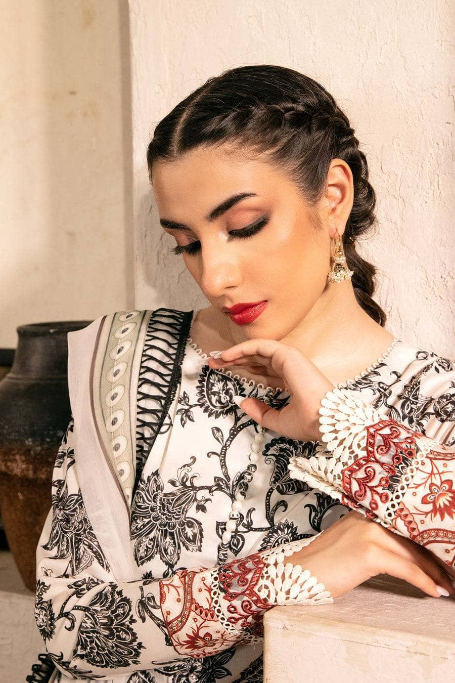 Woman wearing a traditional outfit with intricate patterns, sitting against a neutral background.