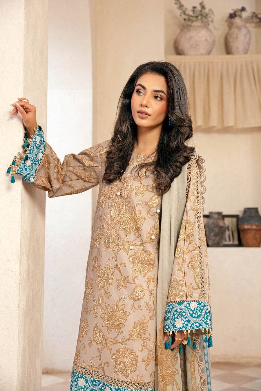 Woman wearing a traditional outfit with floral patterns and blue accents in a neutral setting.