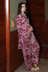 Woman wearing a pink and red patterned outfit standing against a wooden wall.
