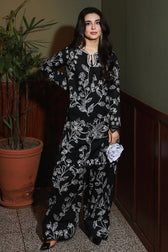 Woman wearing a black floral outfit standing indoors with a plant in the background