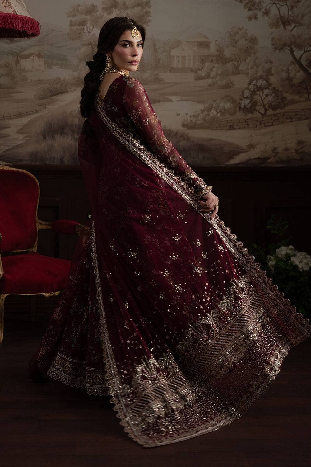 Woman in a burgundy embroidered saree with a classical setting in the background