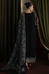 Woman wearing a black dress with a long, patterned scarf draped over her shoulders against a dark curtain background.